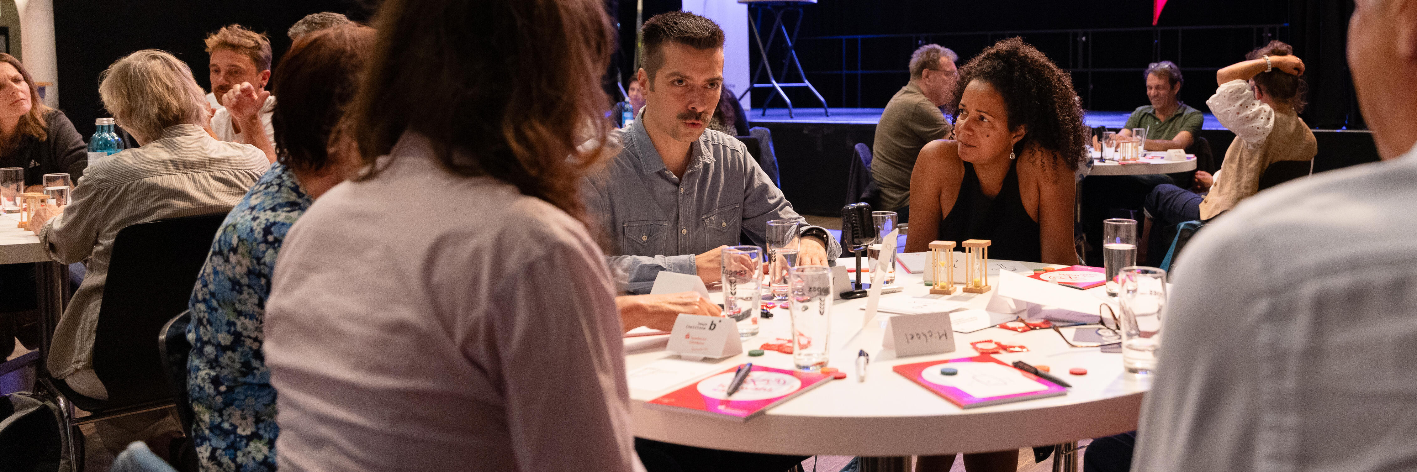 Menschen sitzen an Tischen und spielen das Dialogspiel "Eine Stunde reden"