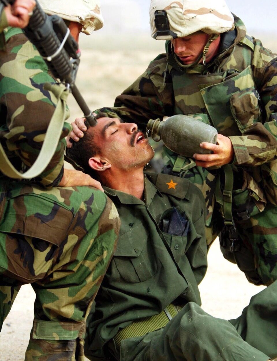 US-amerikanische Soldaten, die einem irakischen Soldaten eine Waffe an den Kopf halten und Wasser geben