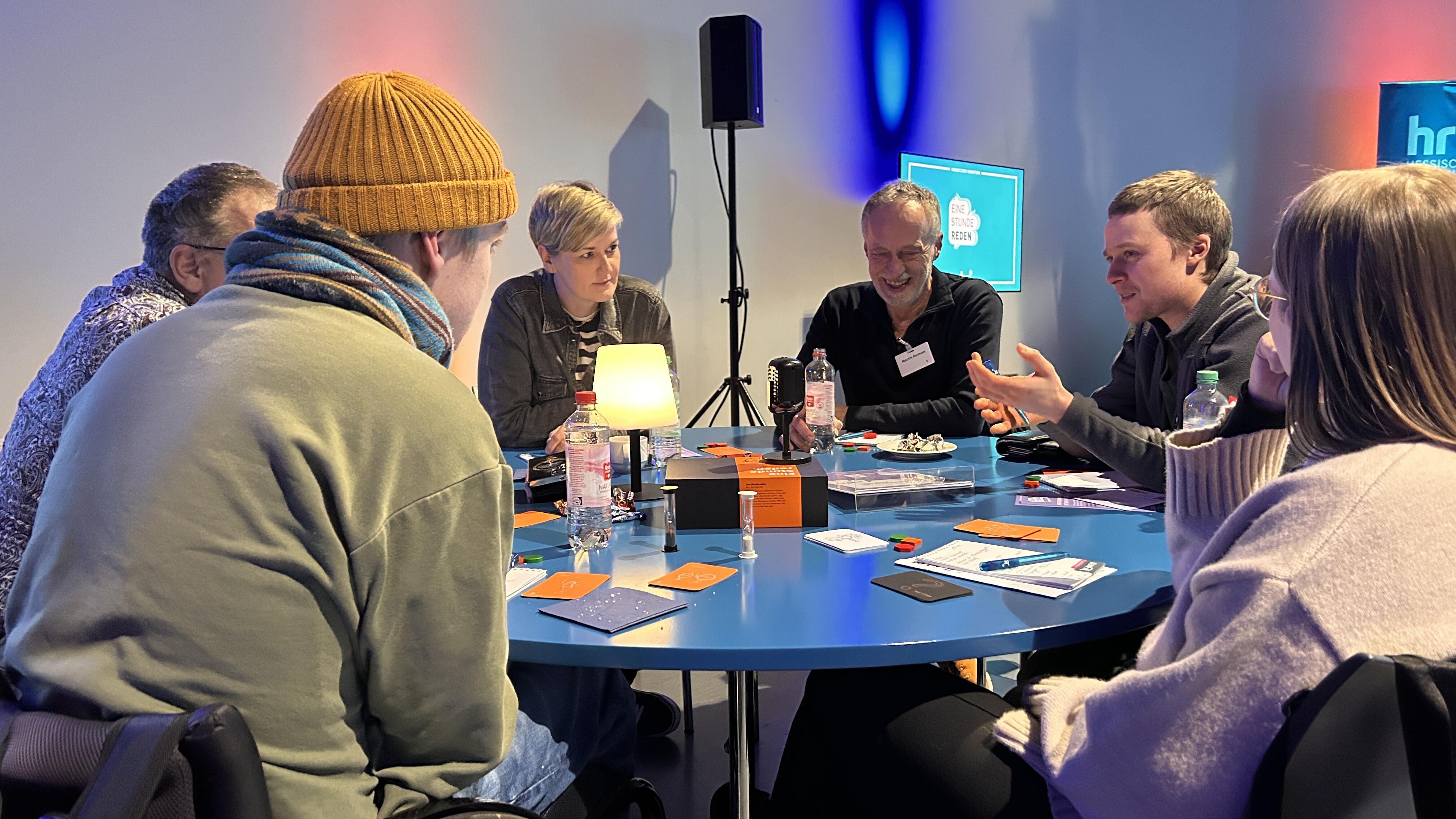 Sechs Menschen sitzen an einem runden Tisch und spielen "Eine Stunde reden" in Kassel.